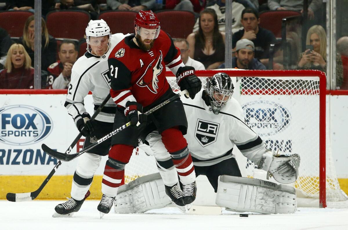 Kings goaltender Jack Campbell, right, makes a save on a shot as Arizona Coyotes center Derek Stepan (21) battles with Kings defenseman Paul LaDue (2) for position during the first period on Tuesday.