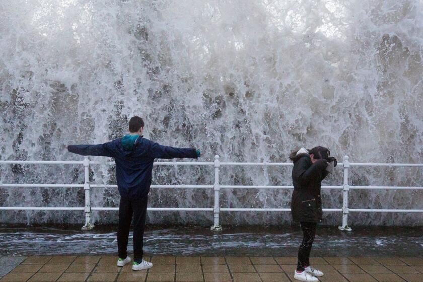 Children stand on the seafront as a wave crashes over the sea wall in Aberystwyth in west Wales as Storm Eleanor lashed Britain with violent storm-force winds of up to 100mph, leaving thousands of homes without power and hitting transport links Wednesday Jan. 3, 2018. (Aaron Chown/PA via AP)