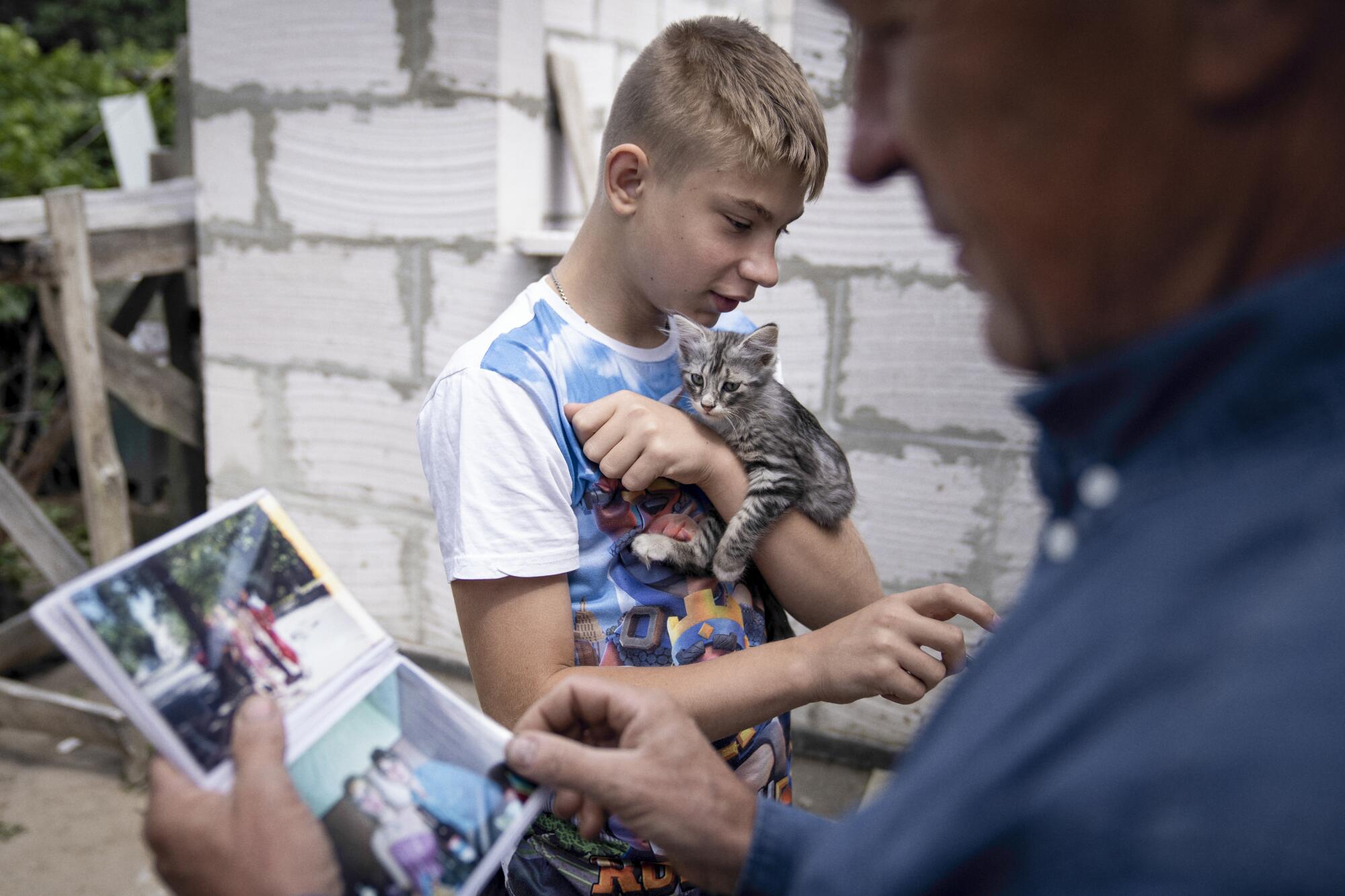 A boy holds a kitten as a man looks at a photo book.