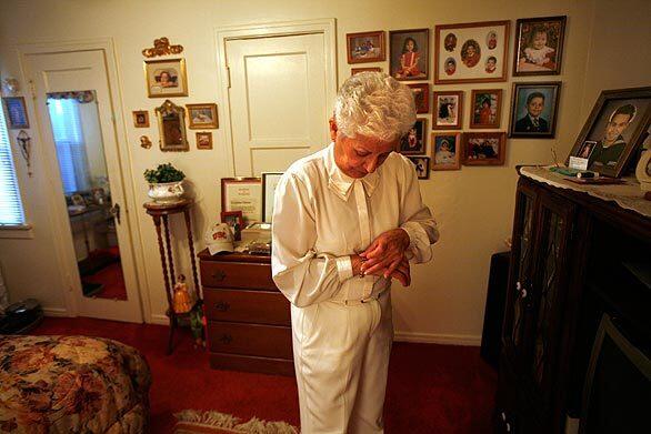 Josephine Chavez, 76, puts on her jewelry before the Christmas dance at the senior center in El Sereno. Behind her are photographs of three generations of her family, including a portrait, right, of her late husband.