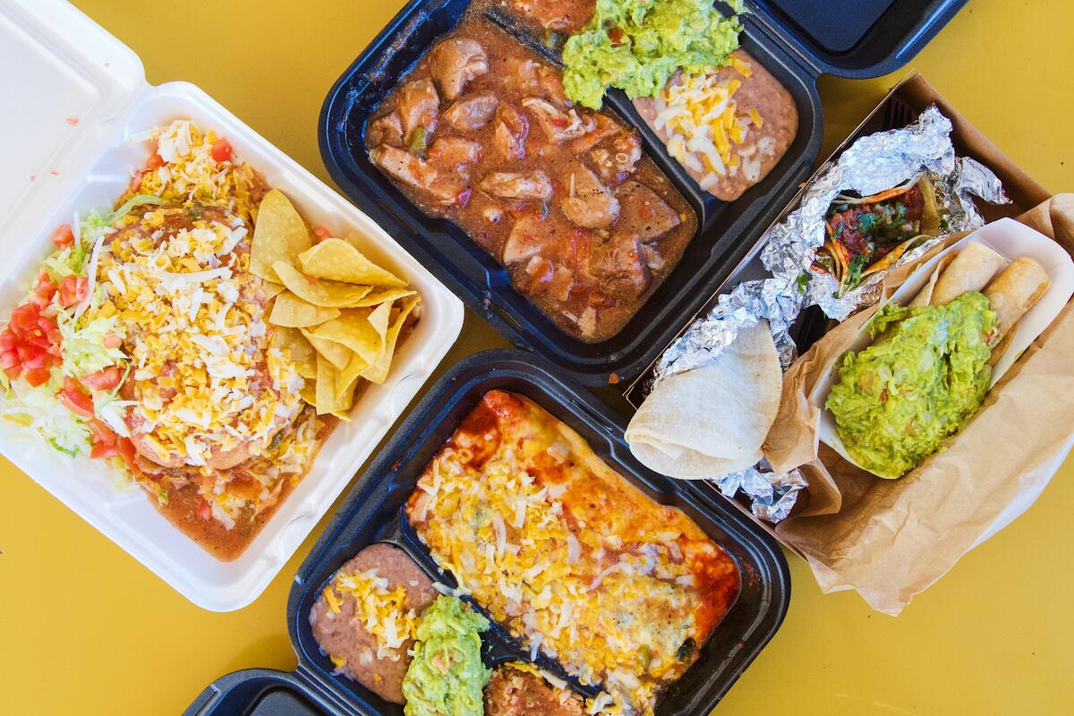 An overhead photo of rolled tacos, an enchilada combo plate and more in to-go containers on yellow tabletop.