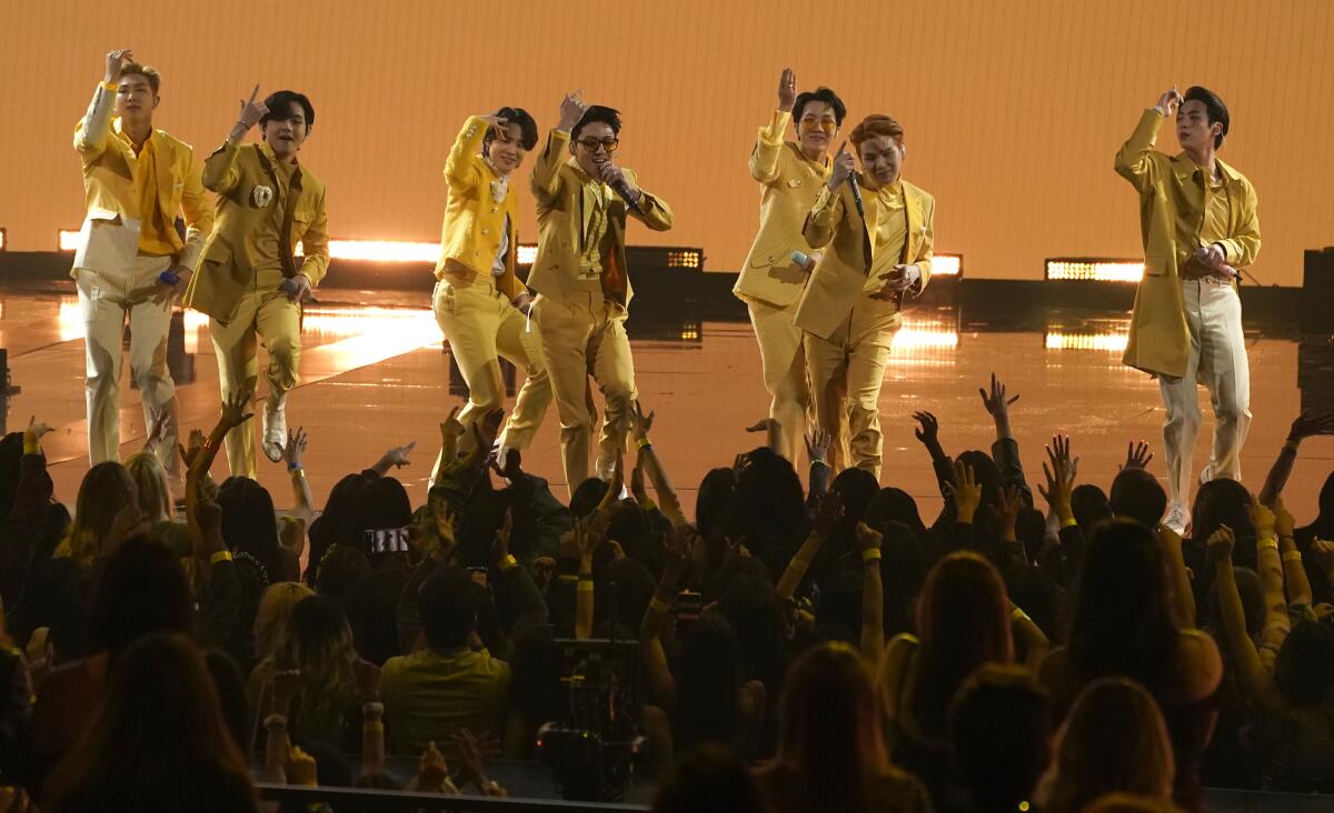 Seven men dance on a stage in yellow suits.