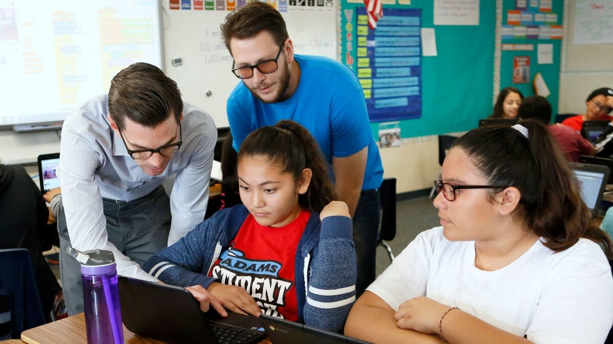 Adams Elementary School Principal Gabriel Del Real, left, and CodeCampus instructor Nathan Valdez go over coding with students Alexis Pellegrin and Laisha Burciaga, right, at the Costa Mesa campus Friday.