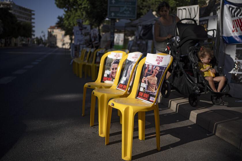 A woman pushes a baby trolley past empty chairs displaying photographs of hostages who were kidnapped during the Oct. 7 Hamas cross-border attack in Israel, set on the street in Jerusalem, Sunday, June 9, 2024. (AP Photo/Leo Correa)