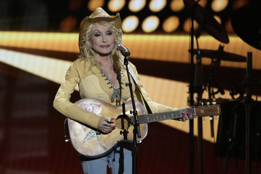 A woman in a yellow cowboy hat plays a guitar onstage at an awards show
