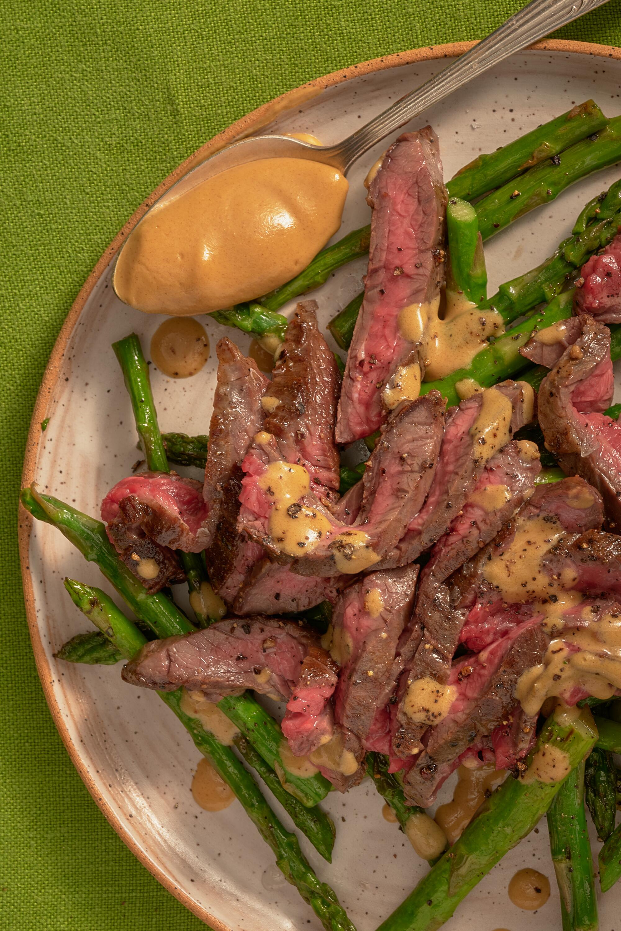 Steak and asparagus on a plate with a spoon holding a dollop of Dijon-soy dressing