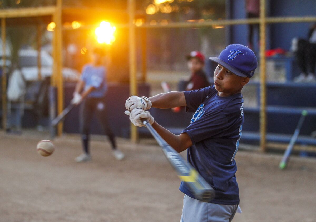 As the sun sets, Municipal de Tijuana team member Aaron Herrera, 12, takes his turn batting during practice at the Liga de Beisbol Infantil y Juvenil Municipal de Tijuana on Friday, July 26, 2019 in Tijuana