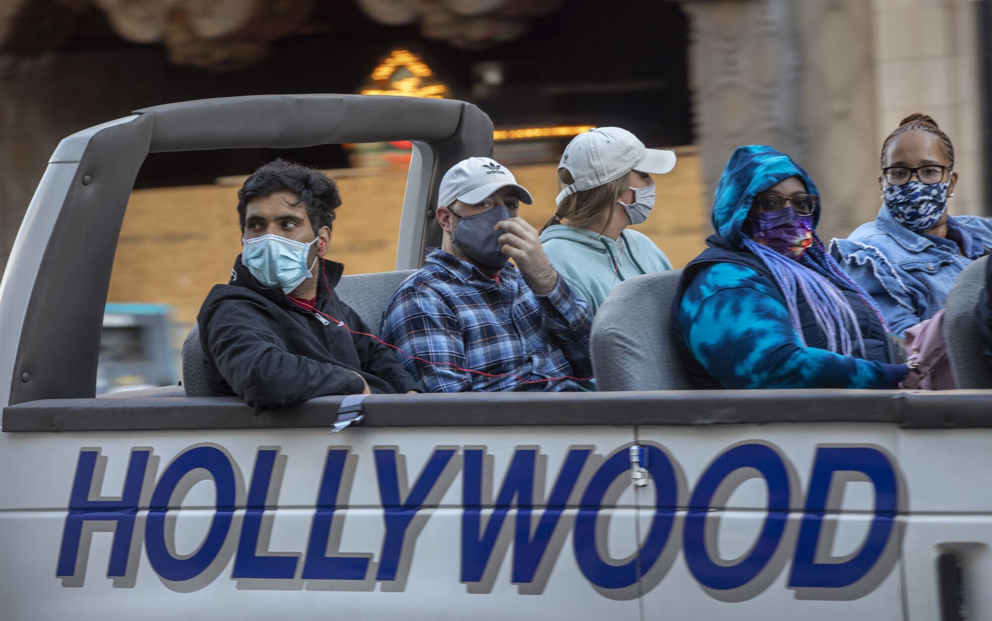 People wear masks on an open-top tour bus with the word Hollywood on the side