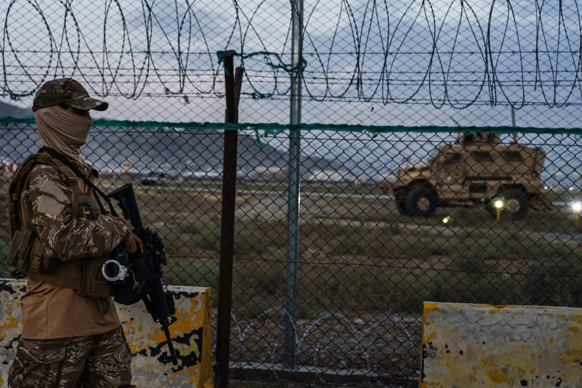 A Taliban fighter walks with a rifle outside a fence