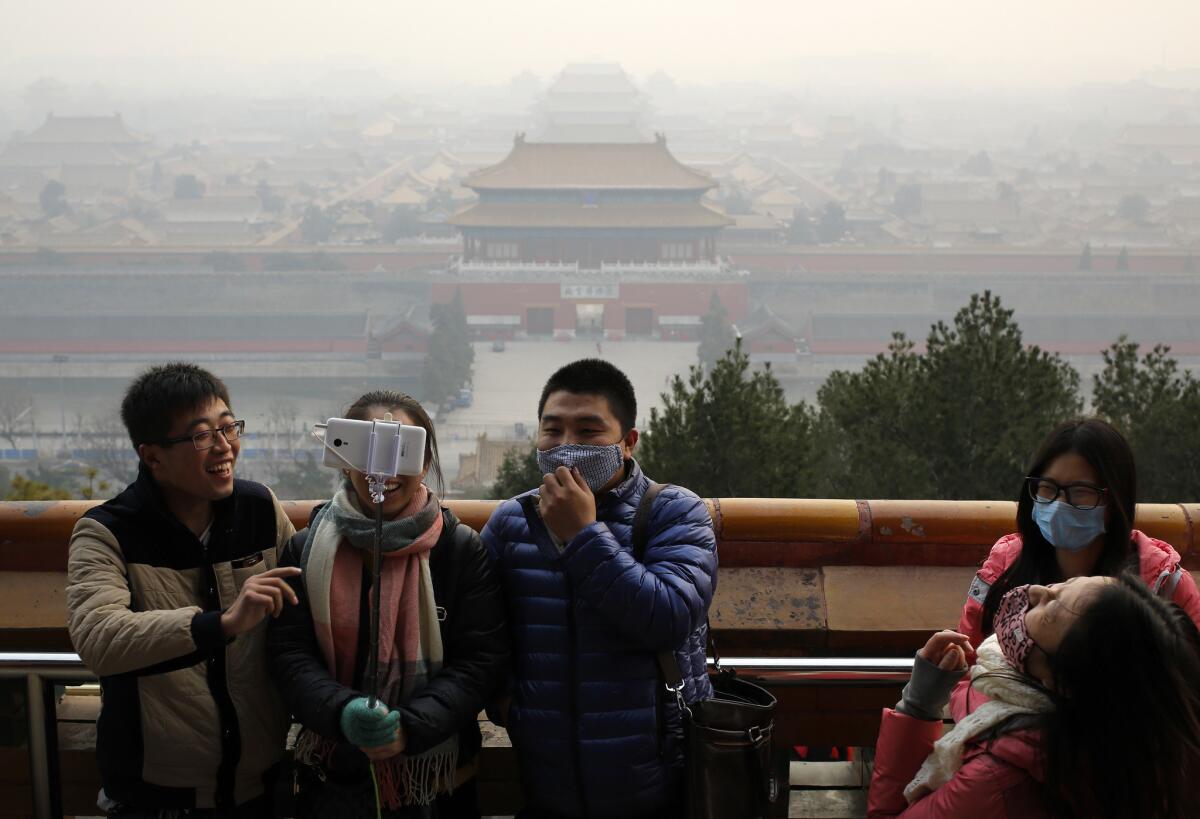 Visitors, some wearing masks to protect themselves from pollutants, take a selfie at Jingshan Park in smoggy Beijing.