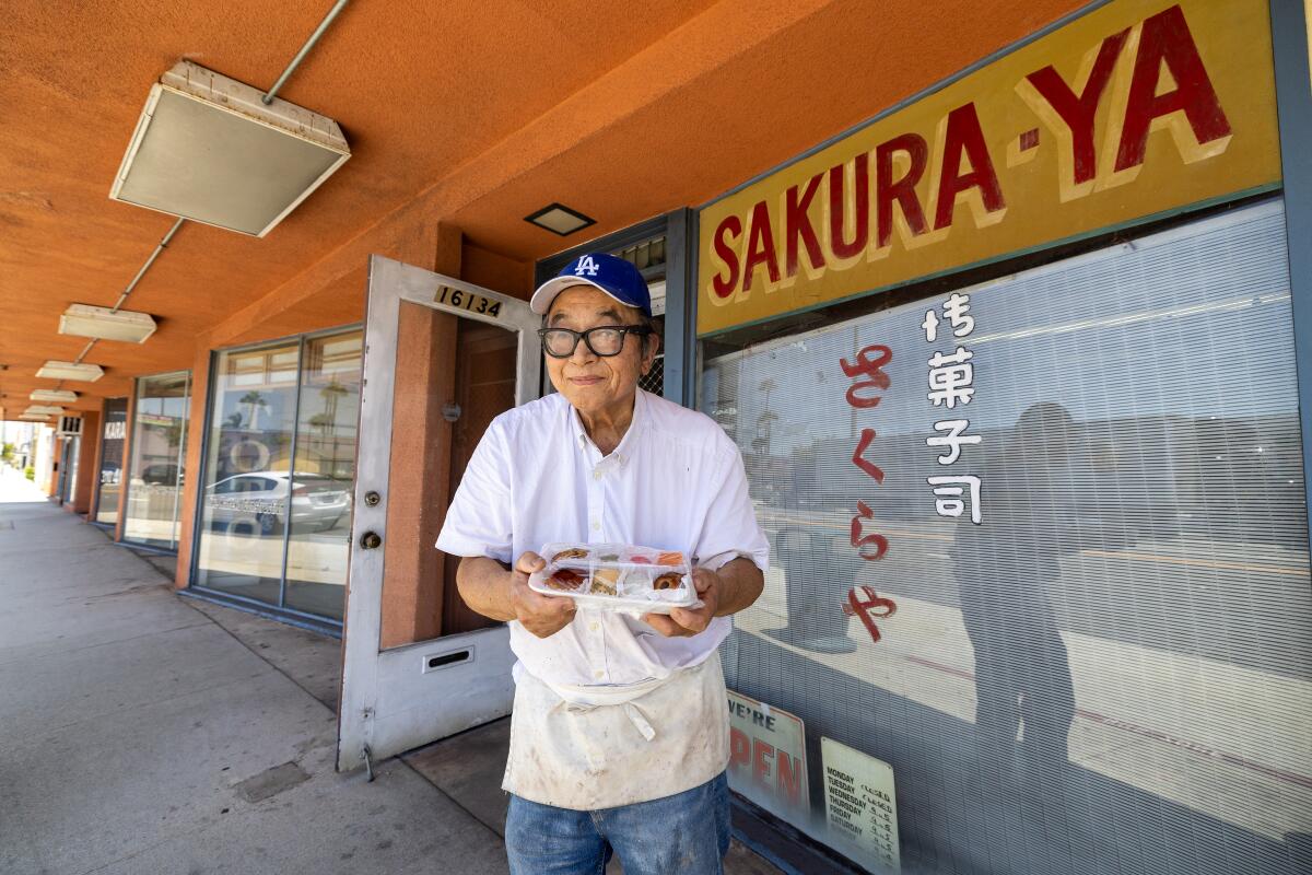 Mas Fujita, wearing glasses, an apron and a Dodger cap, holds a tray of mochi outside his shop on Western Avenue in Gardena