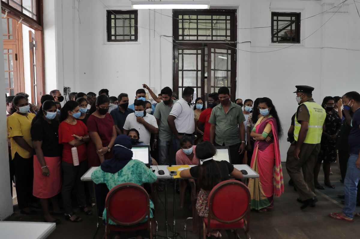 Employees of Colombo municipal council crowd around a table to give their swab samples to test for COVID-19 in Colombo, Sri Lanka, Wednesday, Oct. 7, 2020. Authorities in Sri Lanka on Wednesday widened a curfew and warned of legal action against those evading treatment for COVID-19 after reporting an escalating cluster centered around a garment factory in the capital's suburbs. (AP Photo/Eranga Jayawardena)
