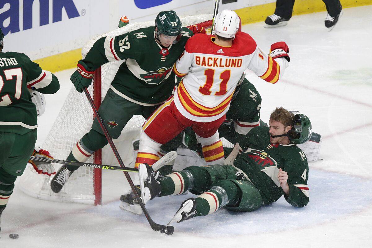 Calgary Flames center Mikael Backlund (11) is denied at the net by Minnesota Wild center Connor Dewar (52), defenseman Jon Merrill (4) and goaltender Cam Talbot (33) during the third period of an NHL hockey game Tuesday, March 1, 2022, in St. Paul, Minn. (AP Photo/Andy Clayton-King)