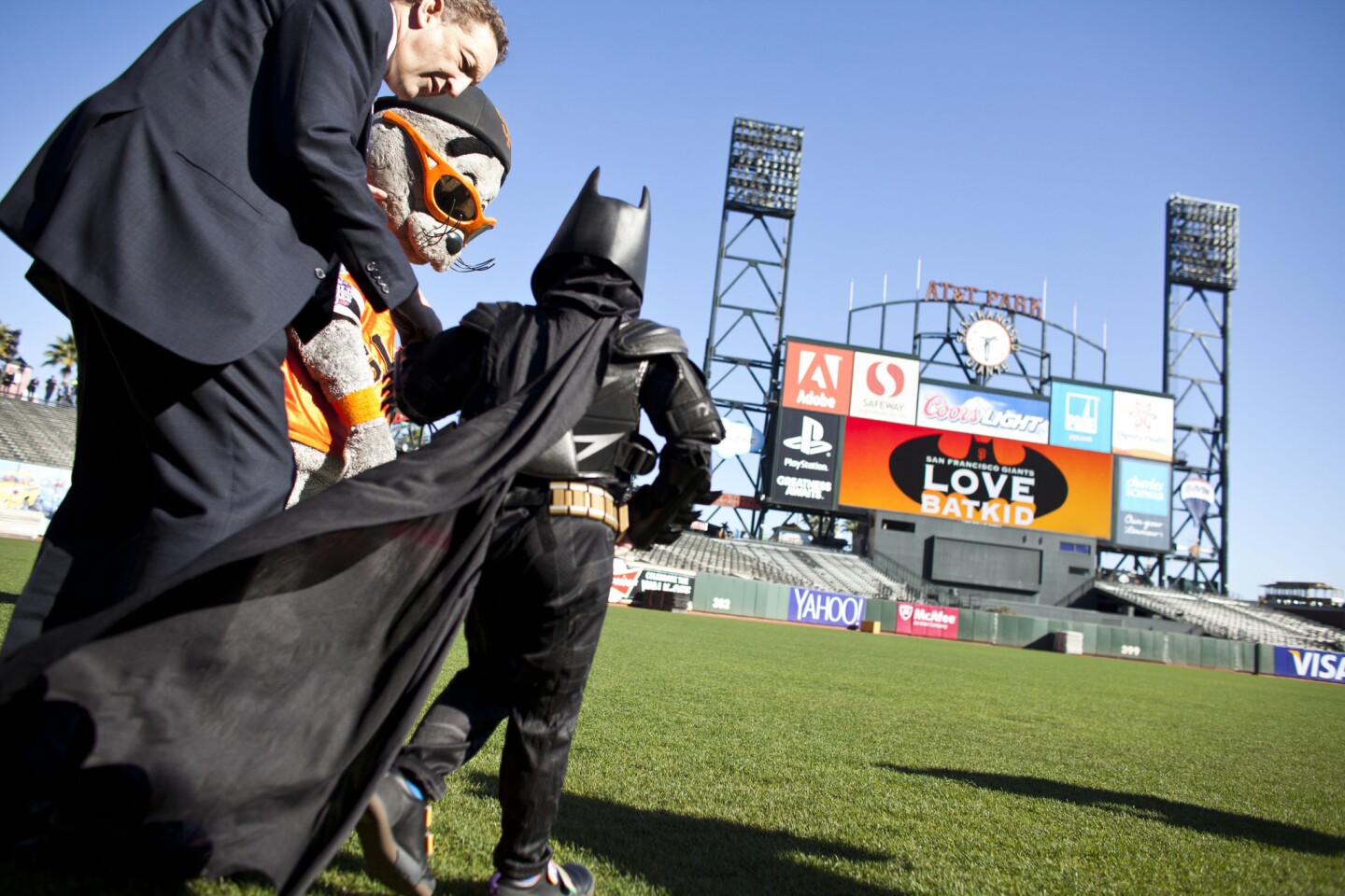 Larry Baer, chief executive of the San Francisco Giants, and the team's mascot, Lou Seal, escort Batkid to the outfield to see a special message on the scoreboard.