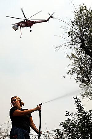 A firefighting helicopter prepares to make a water drop while residents on the ground try to put water on their roofs and surrounding brush in the area of La Ca?ada.