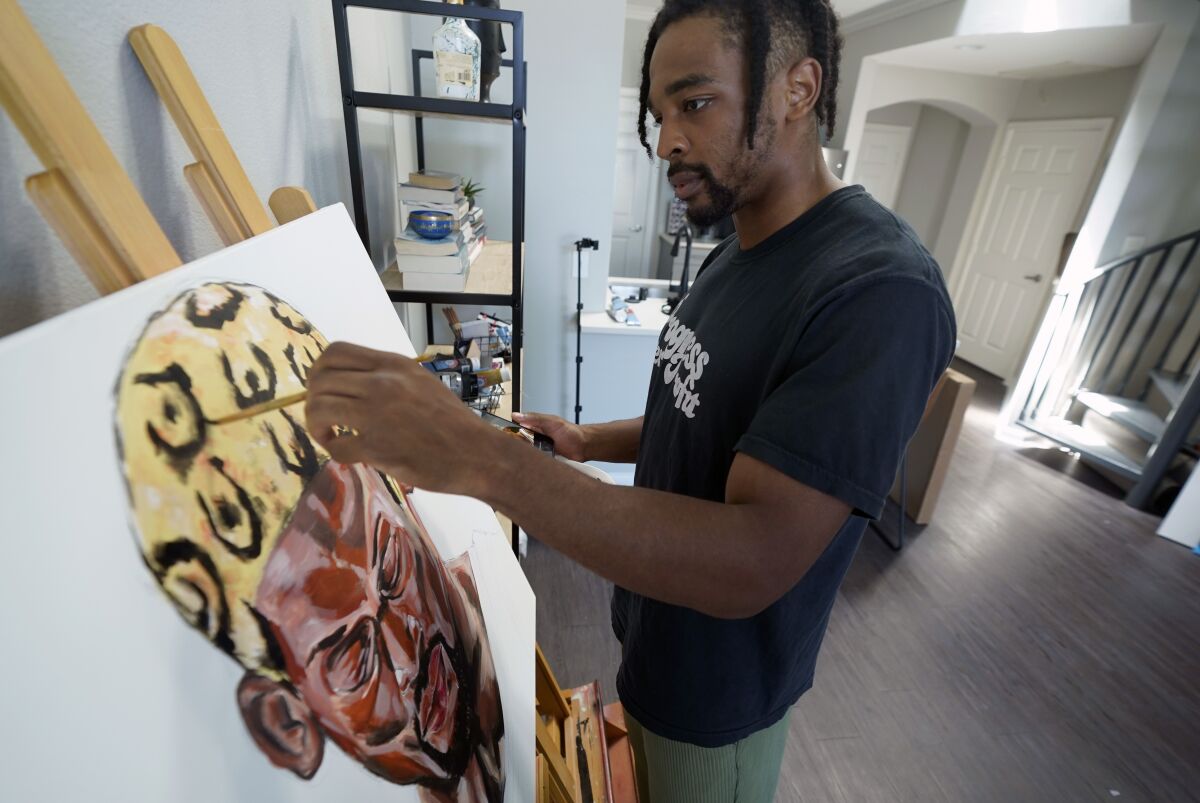 SMU defensive back RaSun Kazadi works on a painting at his apartment Wednesday, Aug. 11, 2021, in Dallas. A junior, Kazadi, who goes by the first name Ra, has been painting only since high school. Some works are lighthearted and fun. Some were done as stress relief. Others reflect a certain point in his life. He also runs a separate non-profit group to promote social justice and community conflict resolution. (AP Photo/LM Otero)