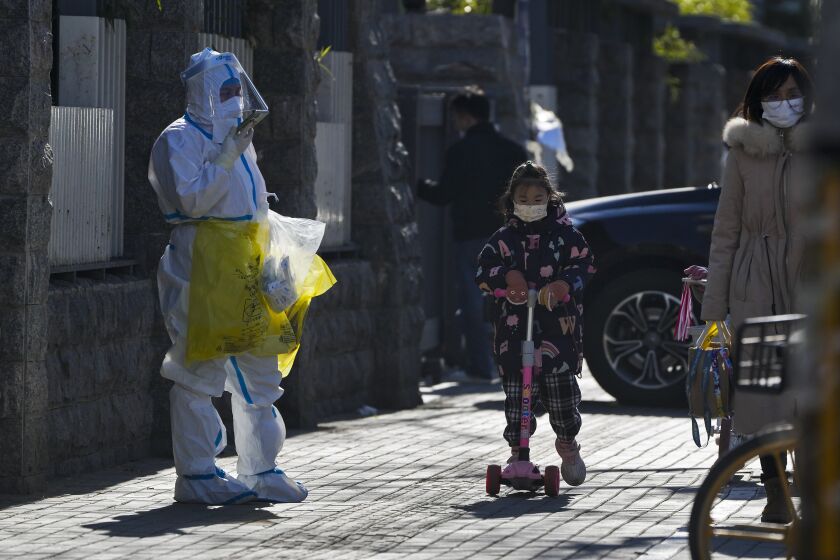 A child wearing a face mask and riding on a scooter passes by a worker in protective suit on his way to collect COVID samples from the lockdown residents in Beijing, Thursday, Dec. 1, 2022. More cities eased anti-virus restrictions as Chinese police tried to head off protests Thursday while the ruling Communist Party prepared for the high-profile funeral of the late leader Jiang Zemin. (AP Photo/Andy Wong)