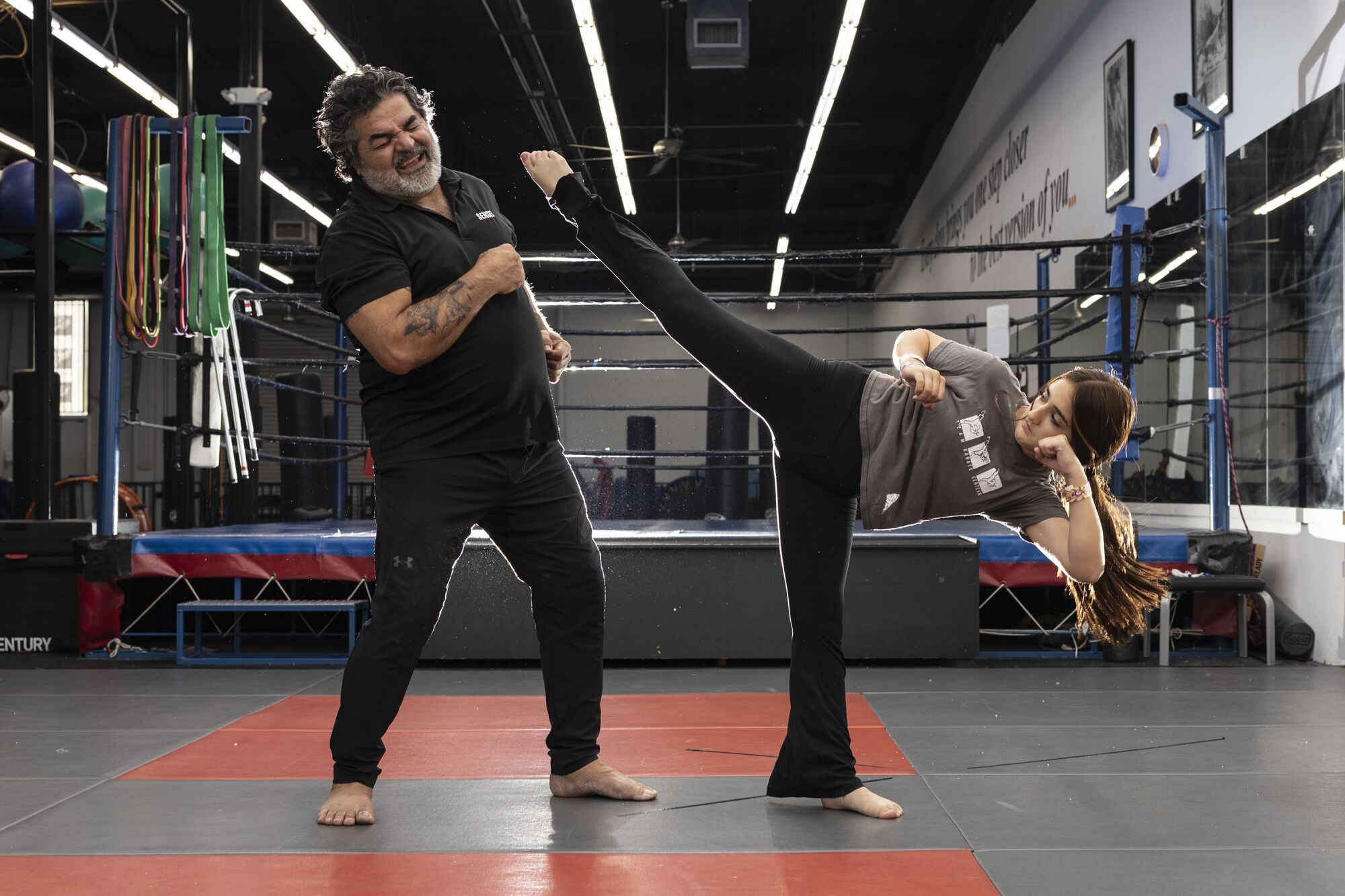 A woman kicks into the air next to a man in a dojo.