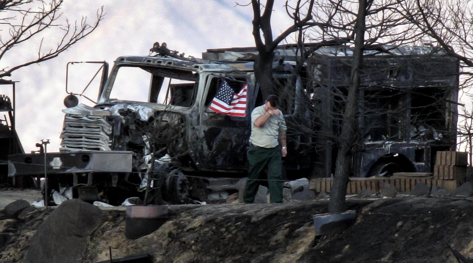 A man  stands by a burned truck and lifts a hand to his face