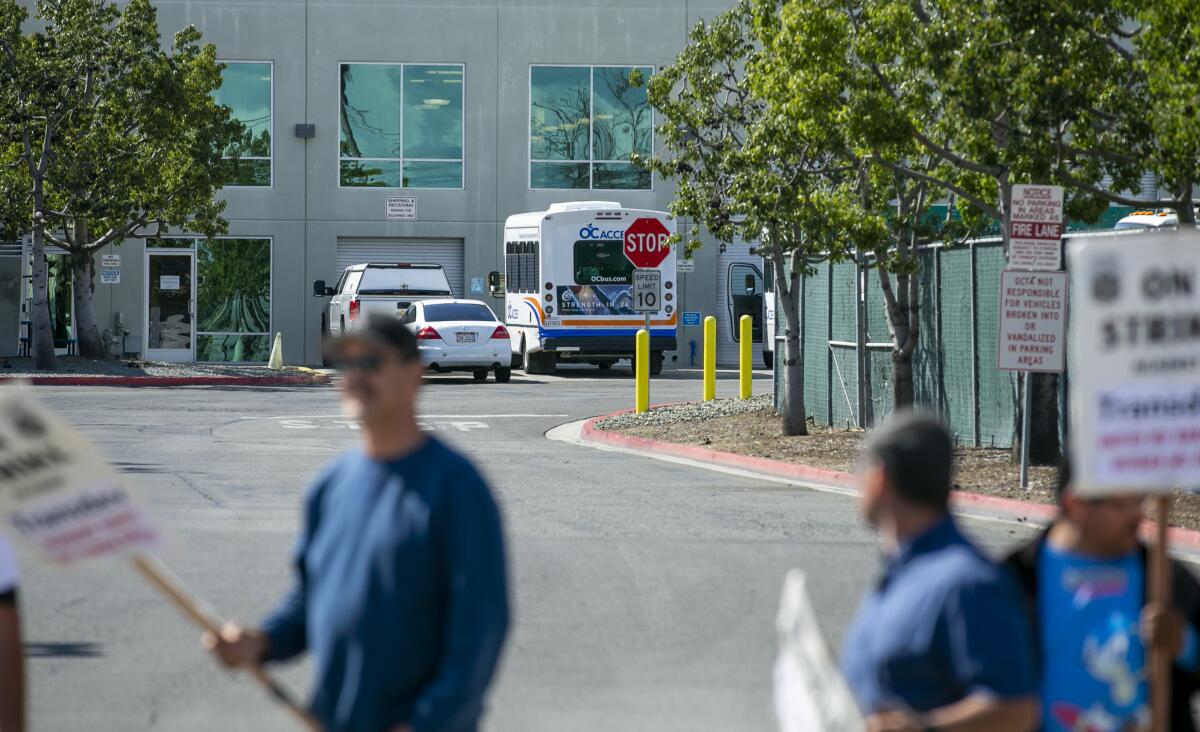 A parked OC ACCESS bus is seen Friday behind picketers at an OCTA bus yard in Irvine.