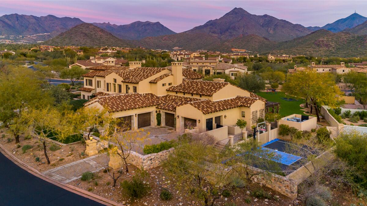 Bird's eye view of property with buildings surrounded by landscaping with hills and other homes in the background.