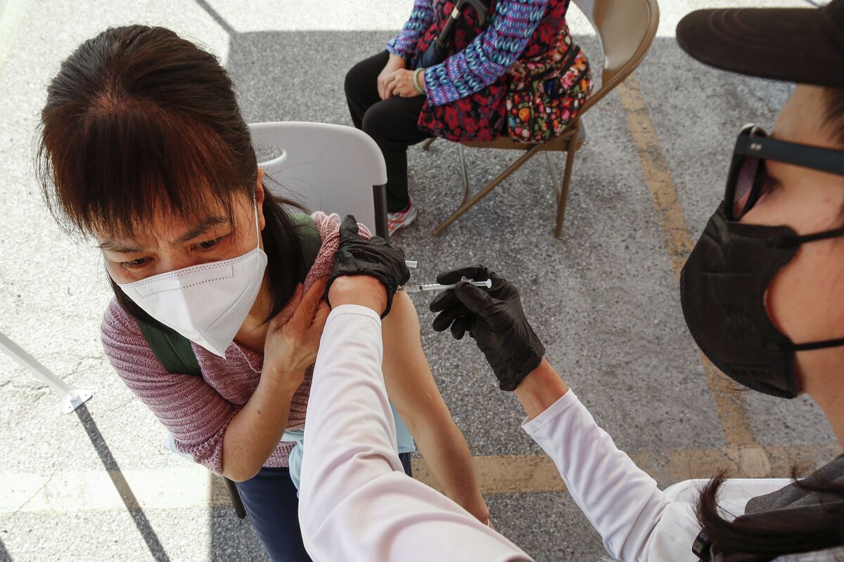 A woman sits on a chair as a health worker administers a shot.