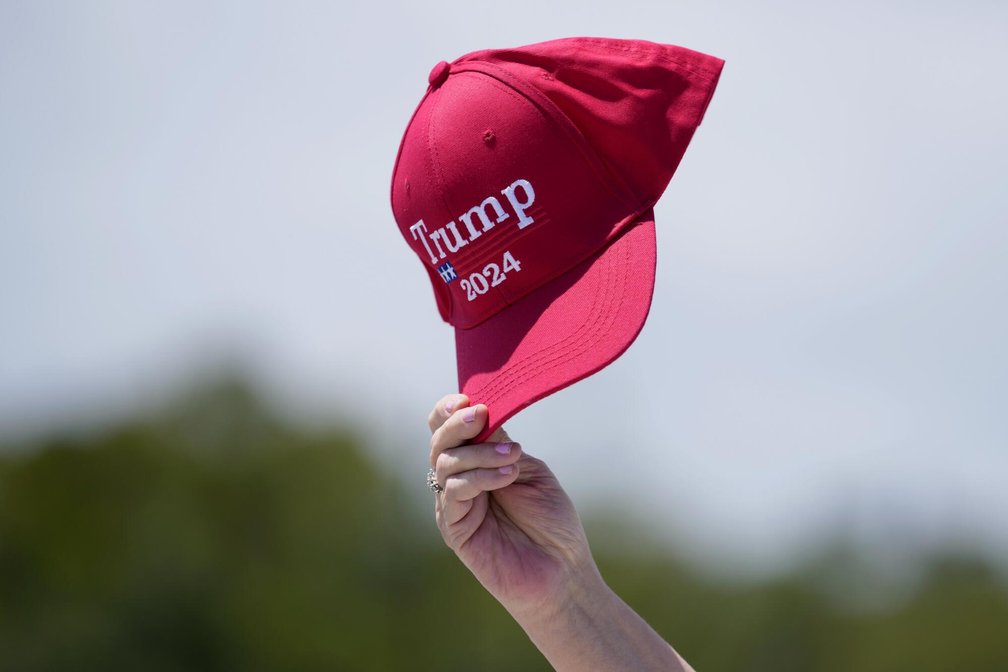 A supporter of former President Trump waves a Trump 2024 hat in the air.
