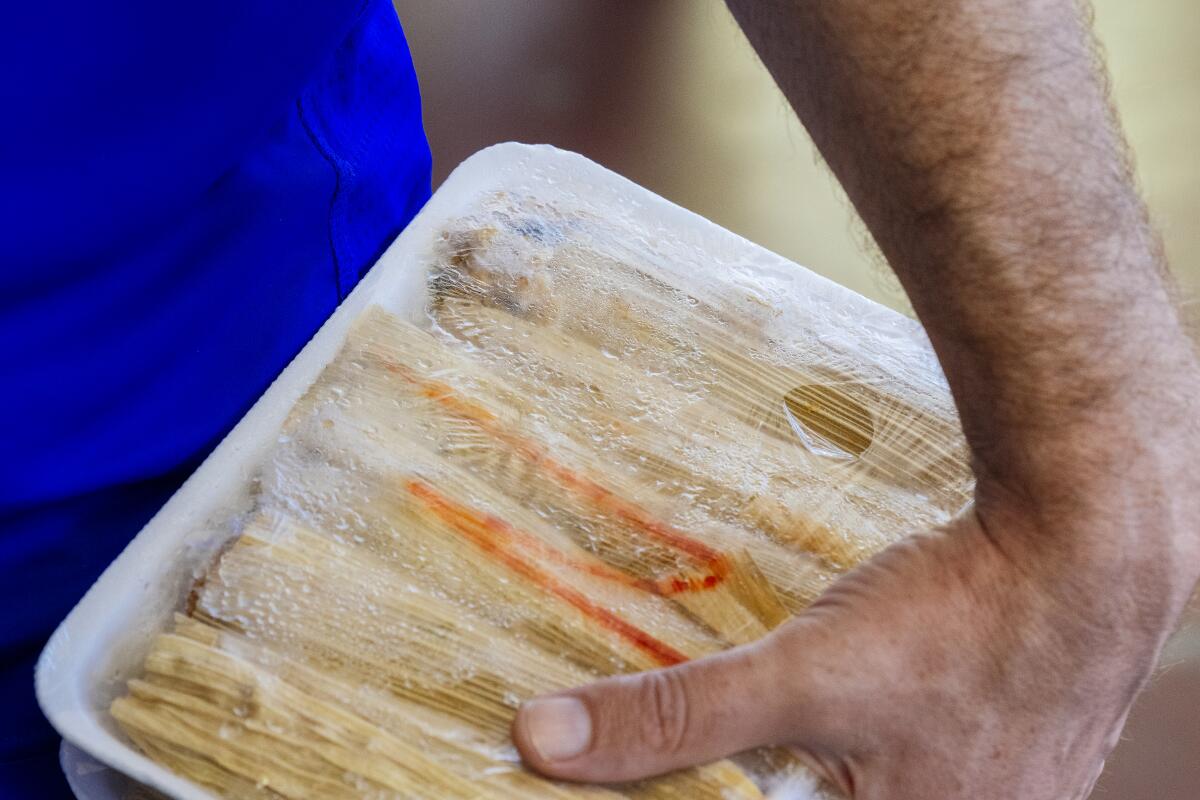 A customer holds a dozen frozen nopales and cheese tamales.