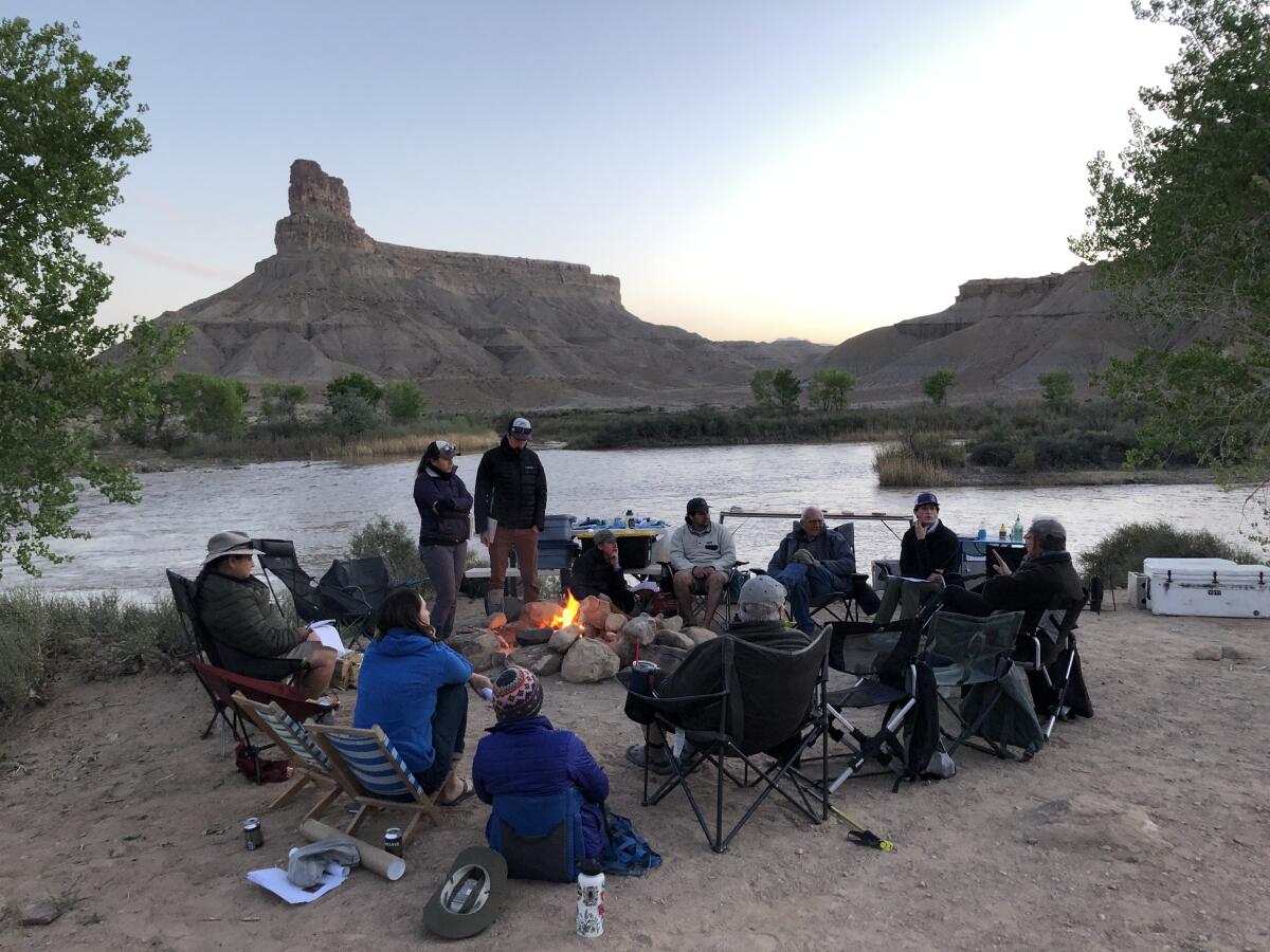 A group of people in camping chairs around a fire next to a river