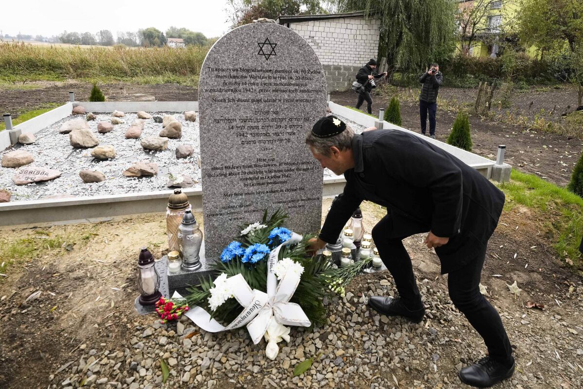 A man lays a candle at a new memorial at a mass grave to some 60 Jews, executed during the Holocaust in Wojslawice, Poland, on Thursday Oct. 14, 2021. It is one of many mass grave sites to be discovered in recent years in Poland, which during World War II was occupied by Adolf Hitler’s forces. (AP Photo/Czarek Sokolowski)