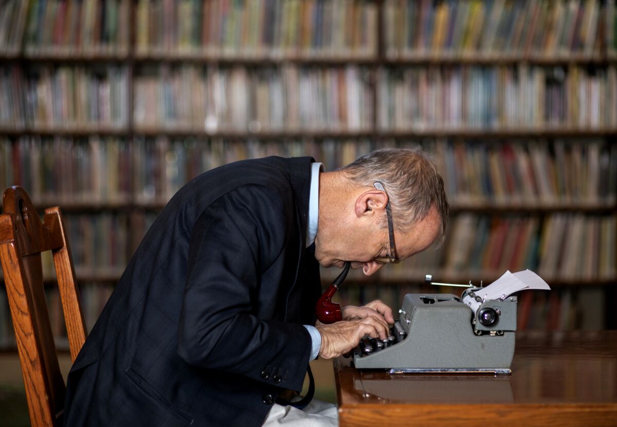 A man leans over a typewriter, his hands on the keys