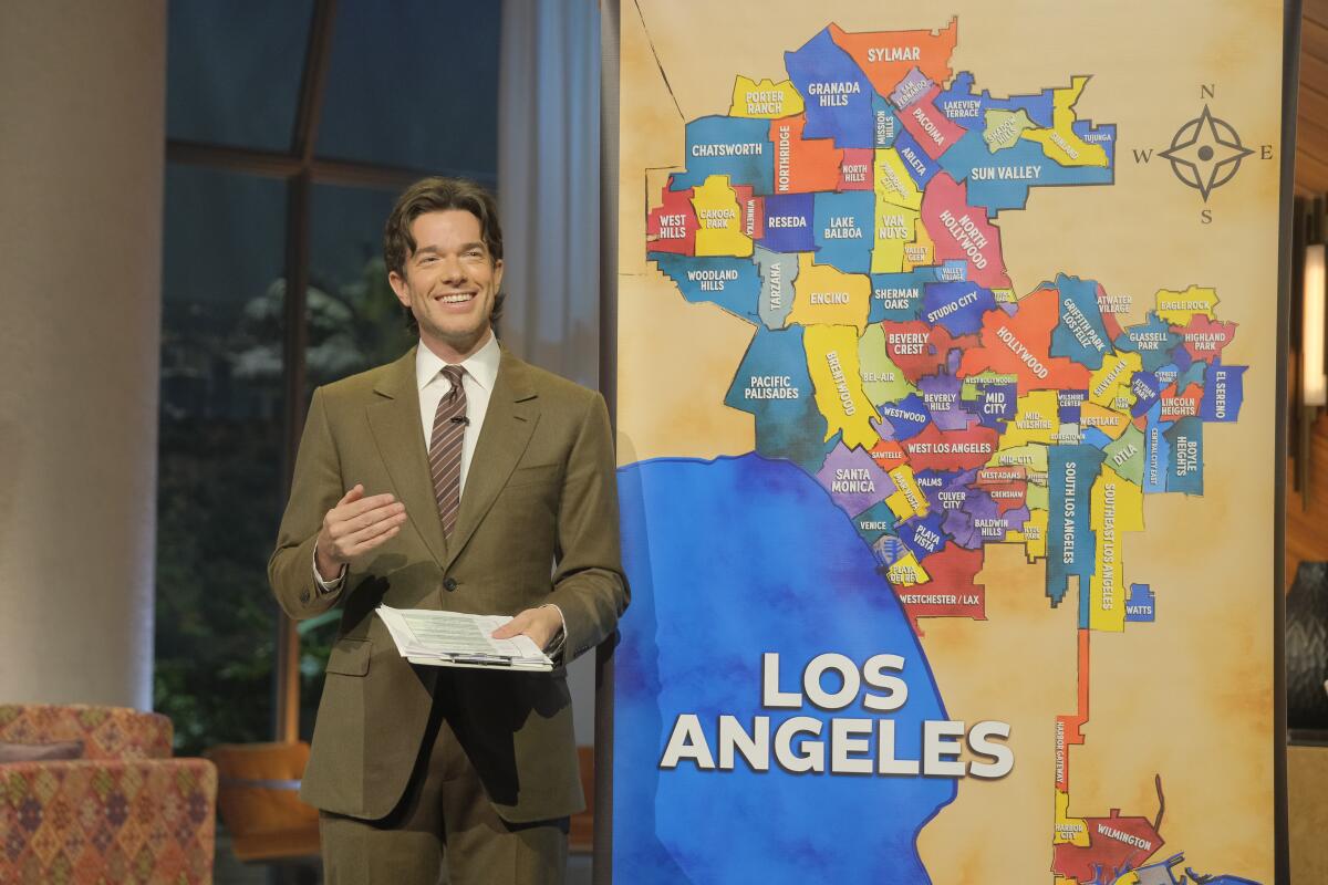 A man wearing a tan suit standing in front of a large map of the city of Los Angeles.