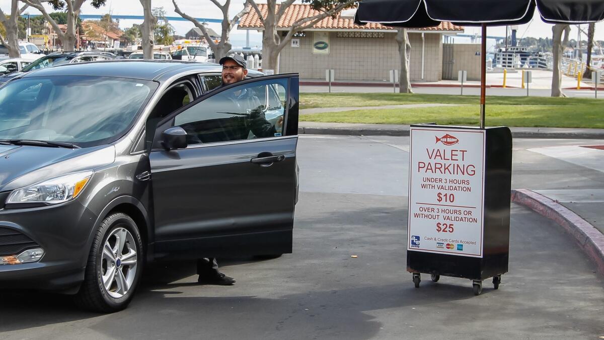 A valet steps out of a car in downtown San Diego. Valets and parking lots are seeing less business as people use ride-hailing services more.