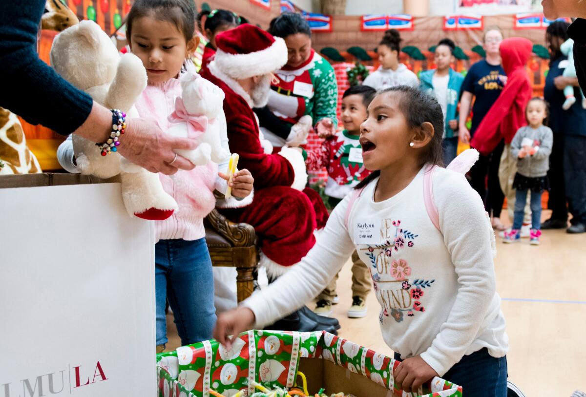 Two girls receive presents in front of long line for Santa Claus