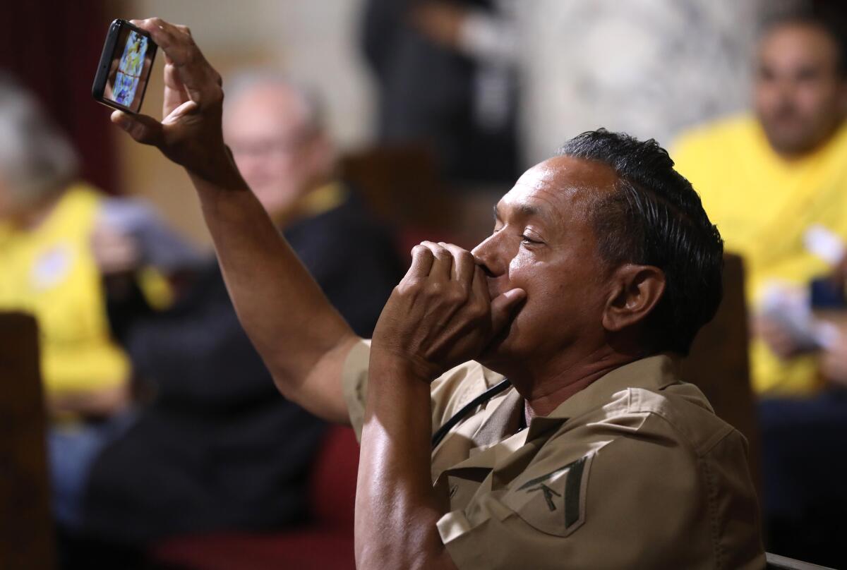A man holds up a phone and cups his free hand to his mouth to amplify his shouting in a crowd