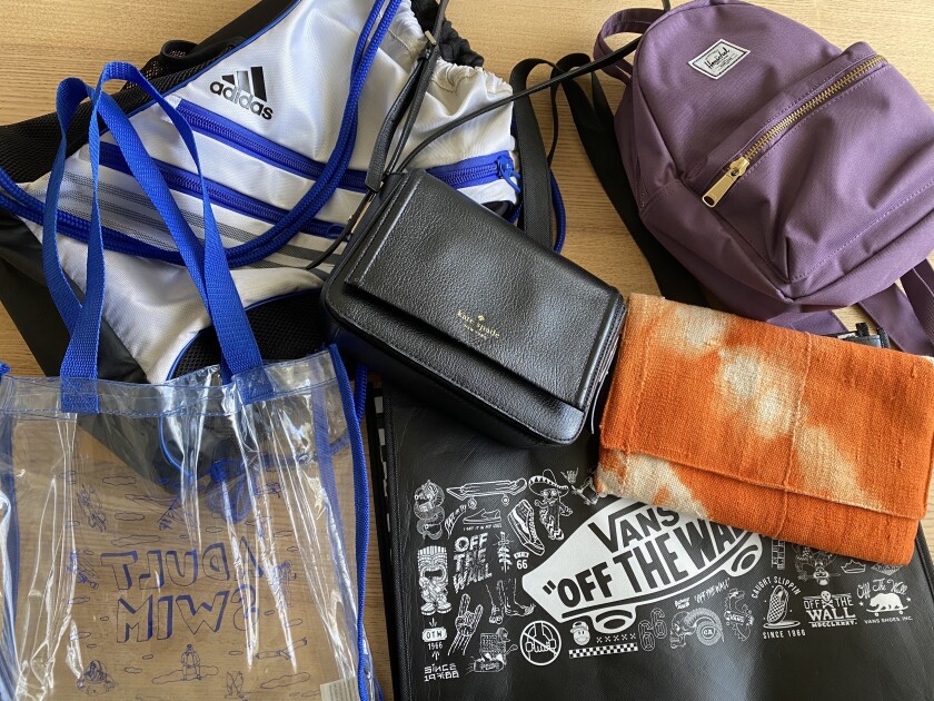 A variety of bags — including totes, a backpack and purses — on a table