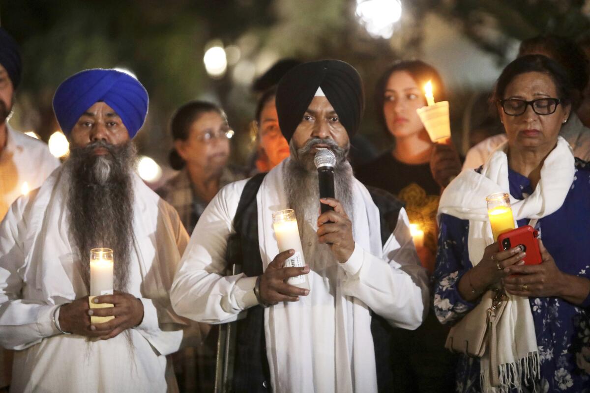 Babaji Karamjit Singh leads prayers while other people stand near him holding candles.