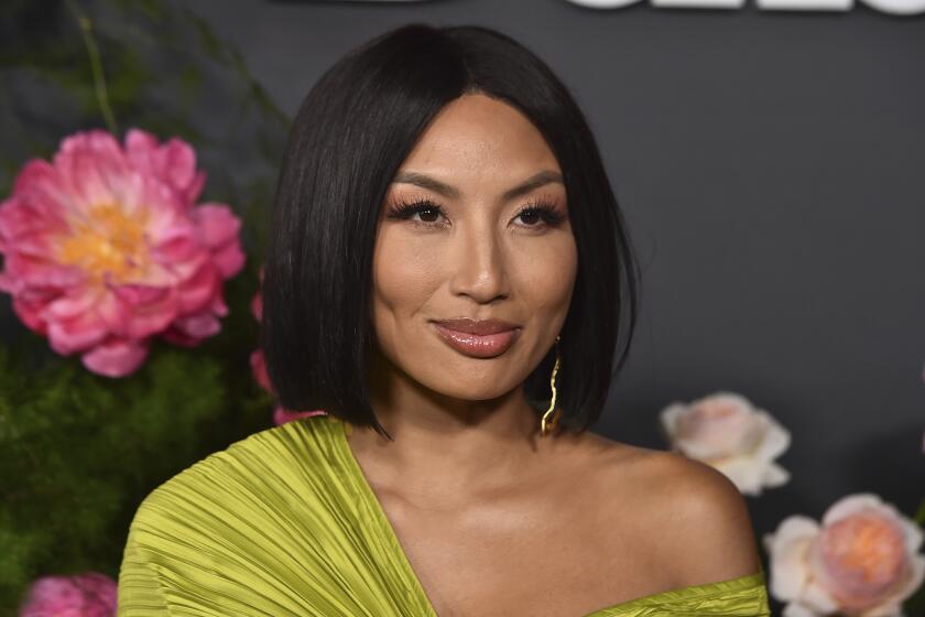 Jeannie Mai poses in a chartreuse-colored gown against a floral backdrop