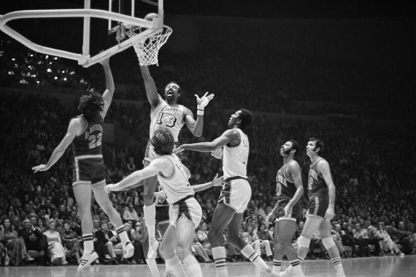 Wilt Chamberlain goes up to tap in a basket for the Lakers against the New York Knicks. Other players are surrounding him.