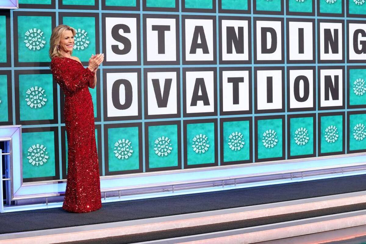 Vanna White standing next to the Wheel of Fortune puzzle board with the words "standing ovation" on it.