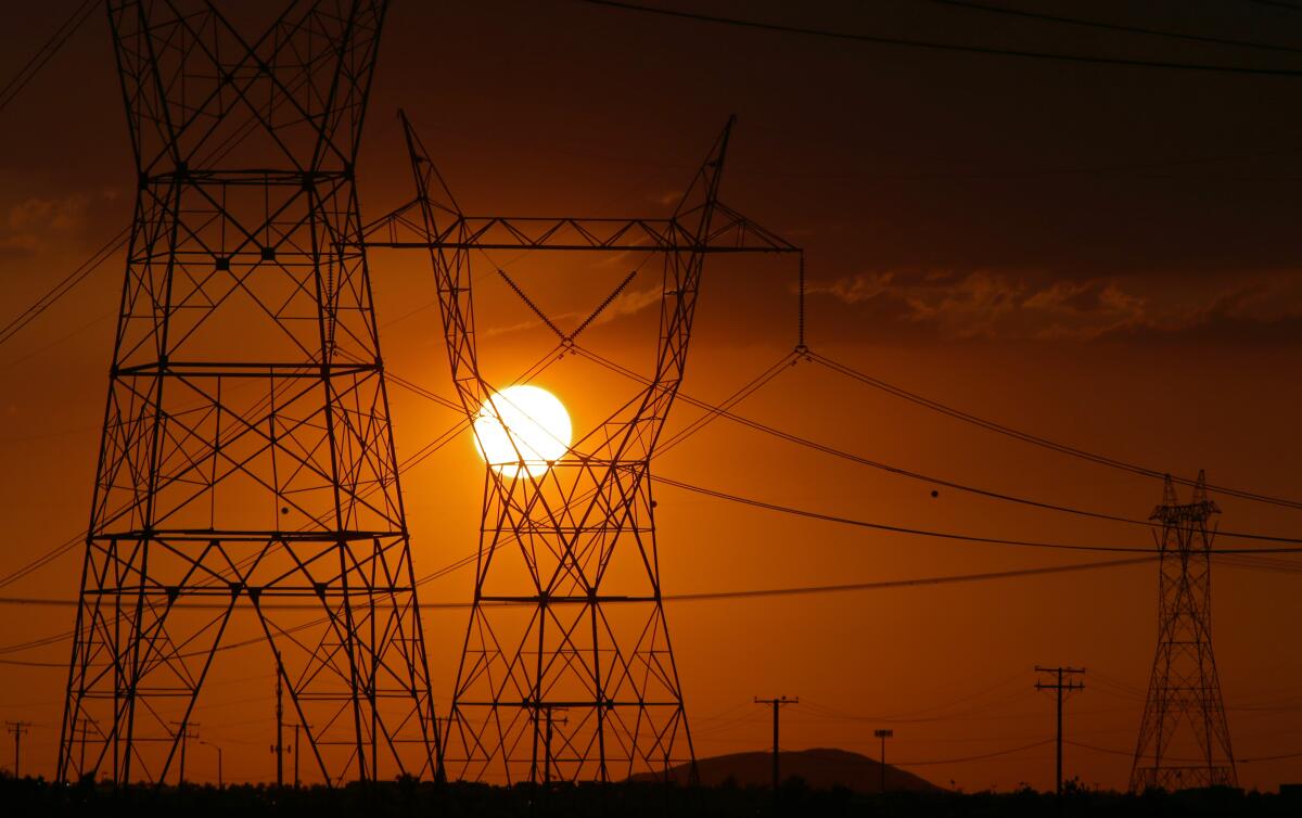 Large towers supporting power lines are silhouetted by the setting sun