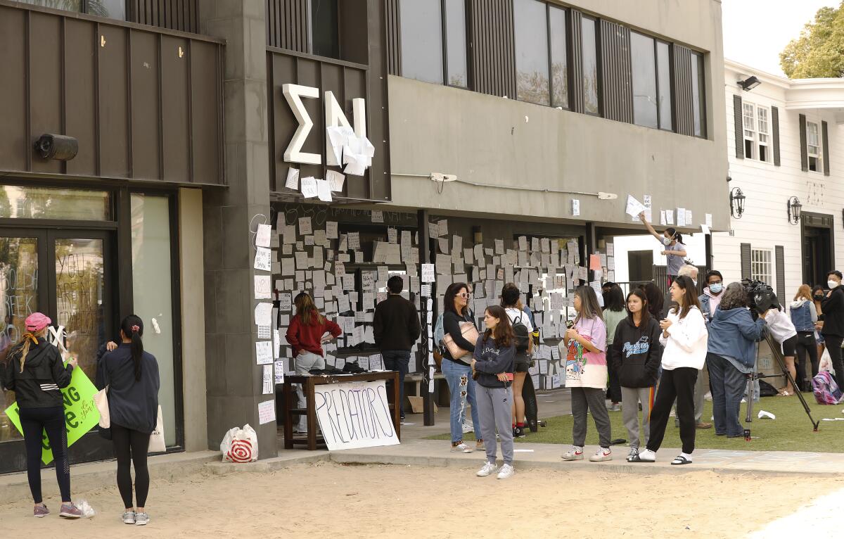 People stand outside a fraternity house that bears the Greek letters Sigma Nu