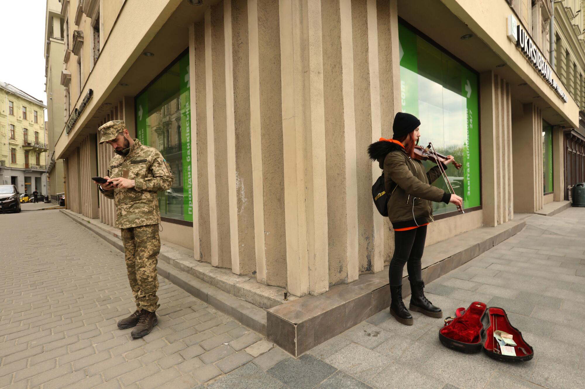 A Ukrainian soldier and a violinist share a corner in downtown Lviv.