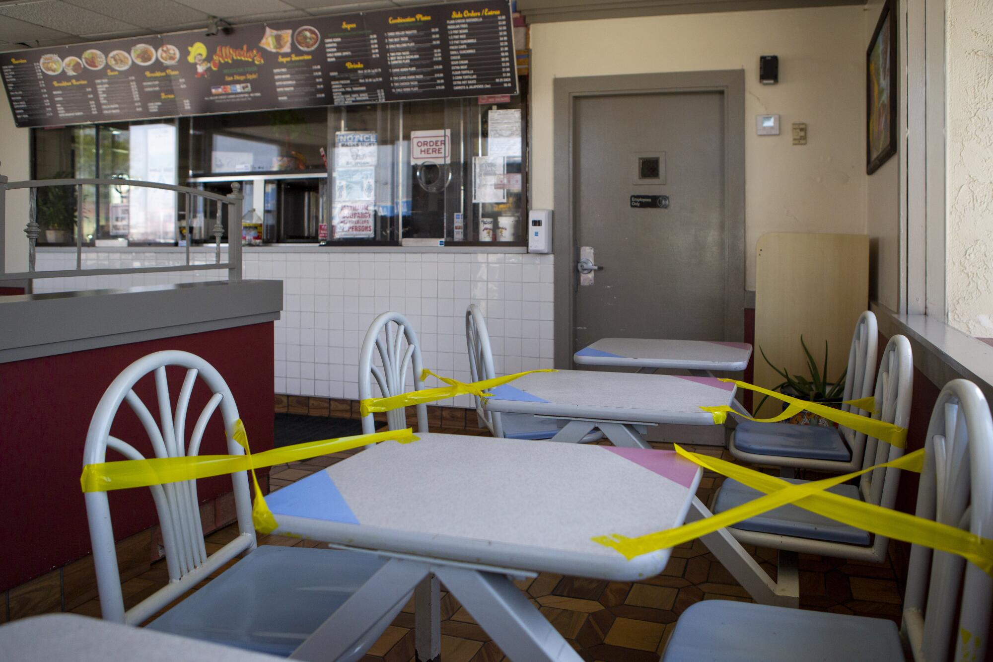 Xs made of yellow tape block off seats at two tables inside a restaurant