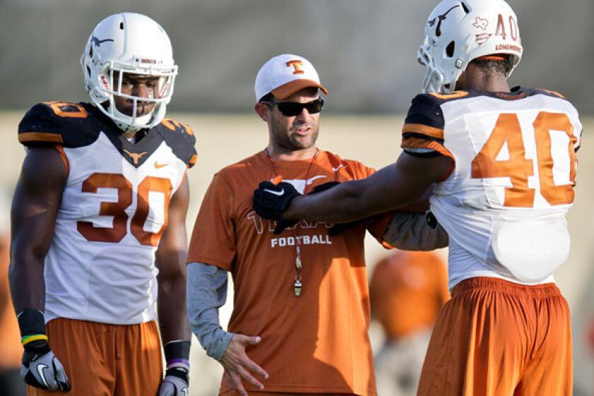 Manny Diaz works with Texas players Timothy Cole, left, and Naashon Hughes during summer camp.