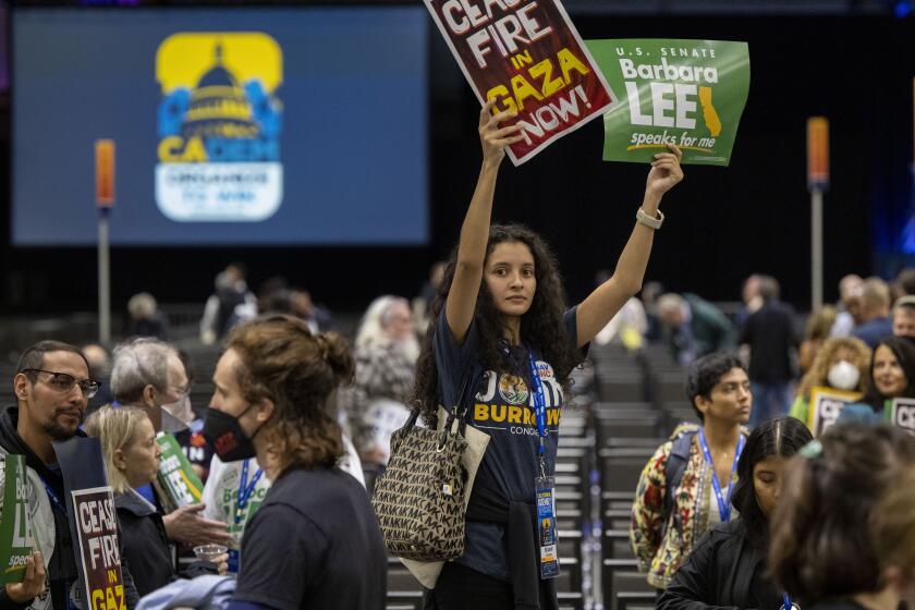 Annamarie Beltran, of the Fresno County Young Democrats, holds up signs as pro-Palestinian demonstrators march inside the session hall during the 2023 California Democratic Party November State Endorsing Convention, Saturday, Nov. 18, 2023, at SAFE Credit Union Convention Center in Sacramento, Calif. (Lezlie Sterling/The Sacramento Bee via AP)