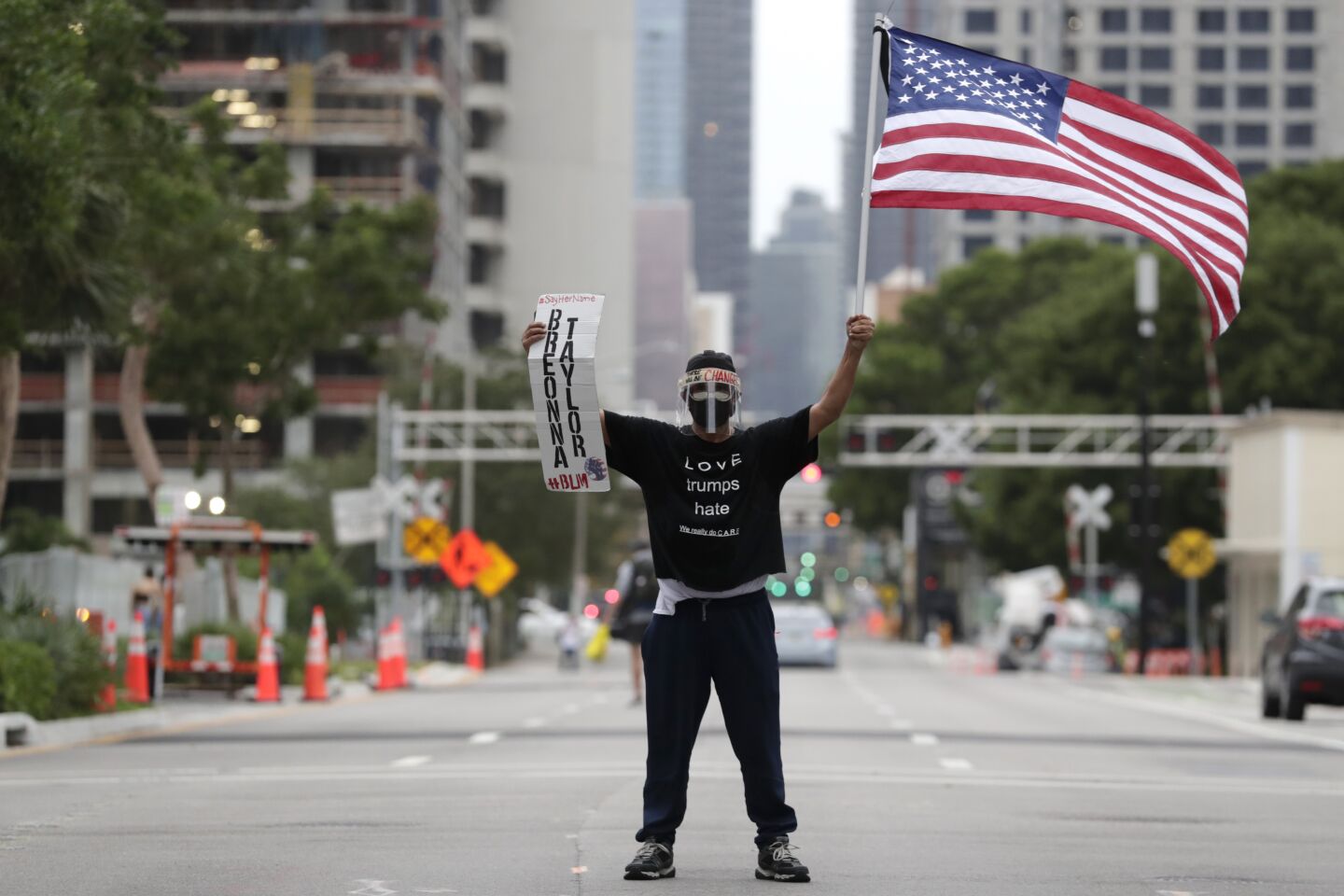 Freddie Peralta stands with the America flag as he holds a sign in memory of Breonna Taylor during a protest in Miami over the death of George Floyd and others, Saturday.