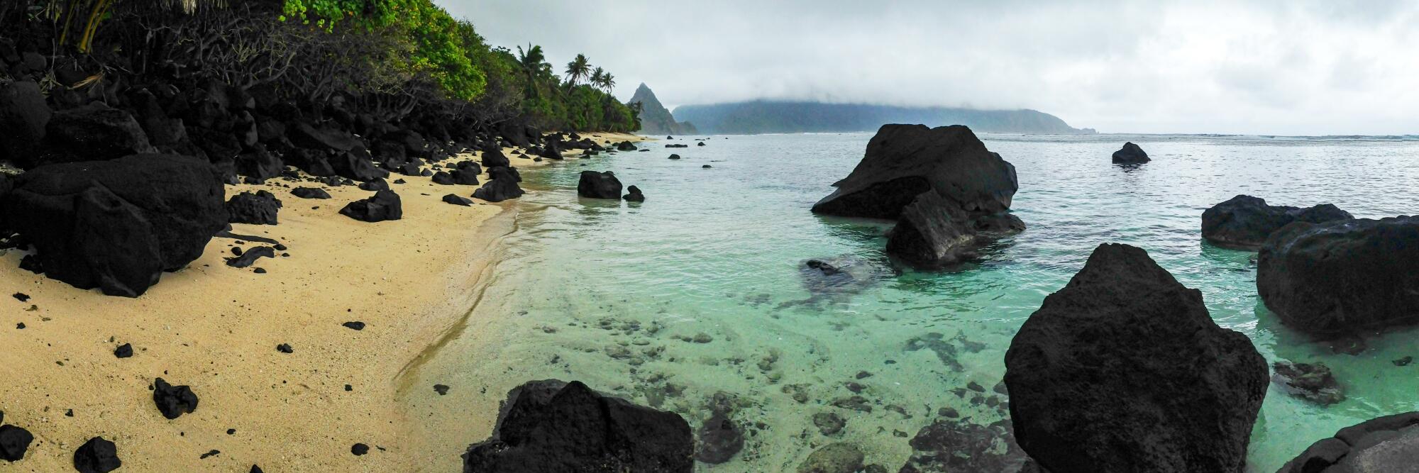 Ofu Beach, American Samoa, with palm trees, sandy area, big rocks and clear water.
