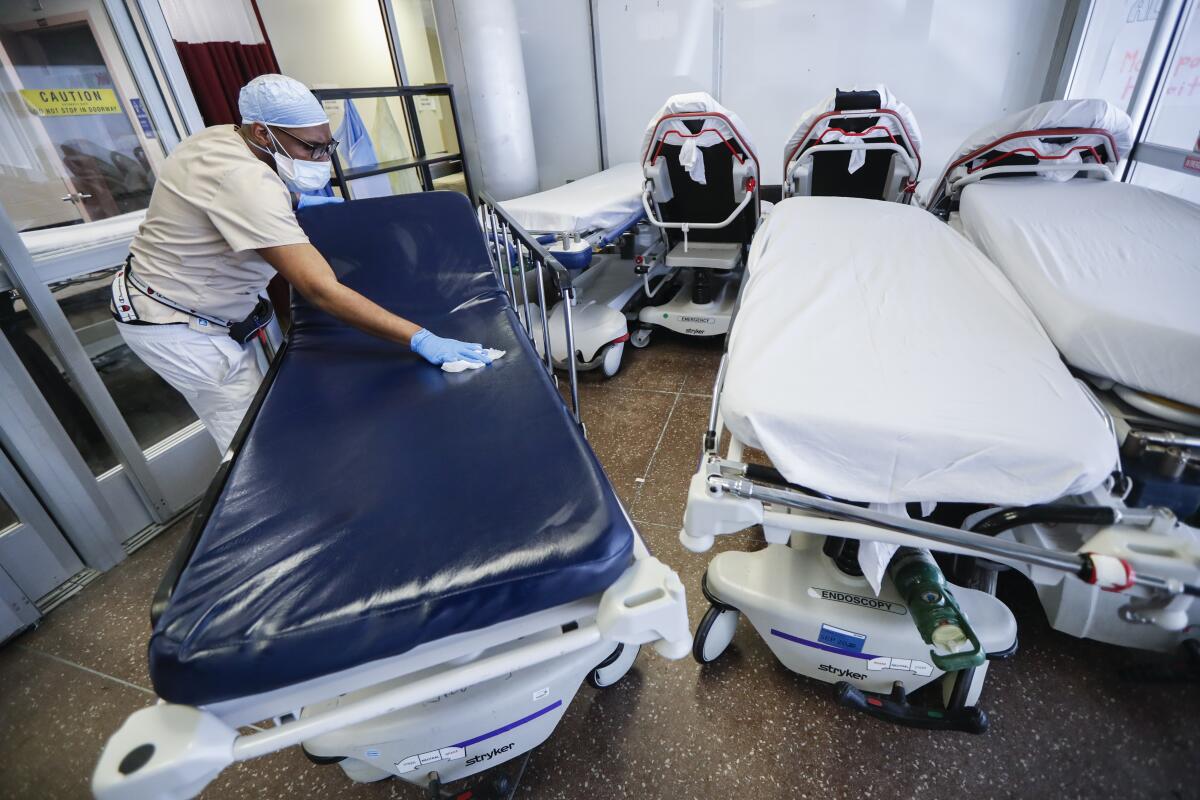 A worker wearing a mask and gloves wipes down a hospital gurney. 