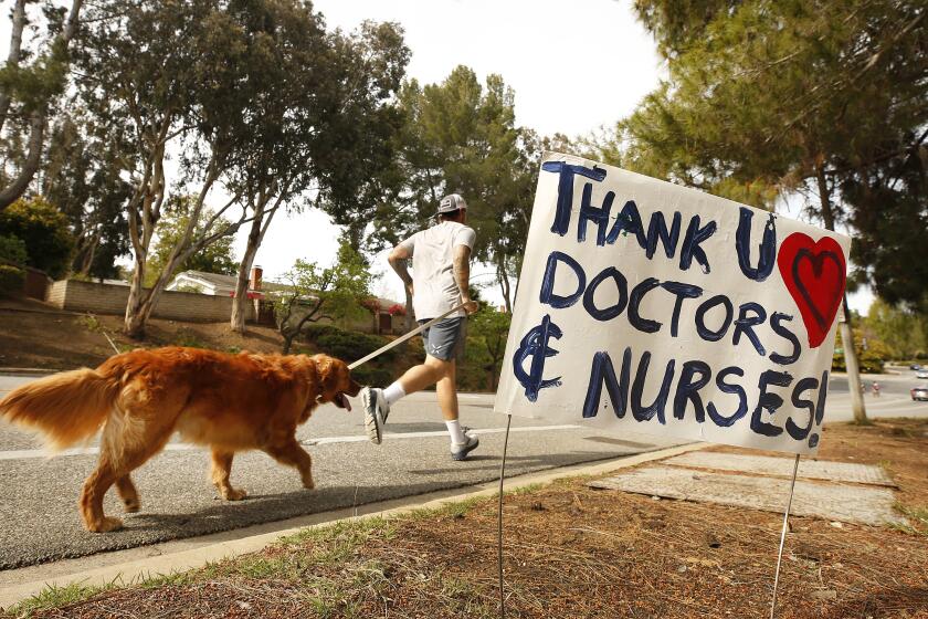 LOS ANGELES, CA - MARCH 31, 2020 A jogger with his dog runs past Los Robles Hospital & Medical Center in Thousand Oaks Tuesday March 31, 2020 where signs of encouragement and praise for healthcare workers battling the coronavirus Covid19 pandemic have been placed along Lynn Road and Janss Road en route to Los Robles Hospital & Medical Center. The signs were created by Trevor Quirk, a Ventura attorney who ran for office, using leftover campaign signs w the "help of a few good friends." We are documenting what our neighborhoods look like in the age of coronavirus Covid19 pandemic. (Al Seib / Los Angeles Times)